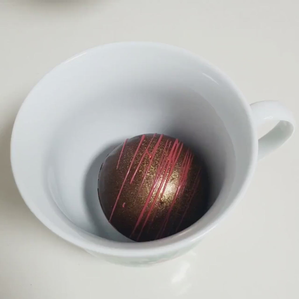 Heiße Schokoladenbomben in der Tasse, heiße Milch wird aufgegossen